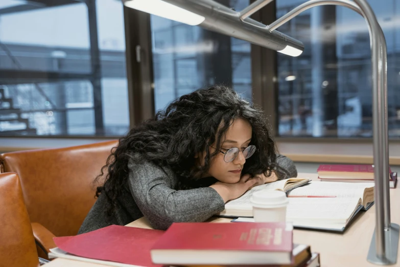 a woman sitting at a table reading a book, a cartoon, by Adriaen Hanneman, pexels contest winner, asleep, imaan hammam, at college, candid shot