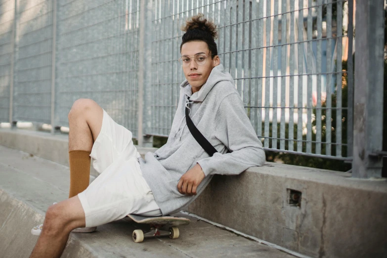 a young man sitting on top of a skateboard, by Emma Andijewska, trending on pexels, realism, grey hoodie, nonbinary model, bra and shorts streetwear, white clothing