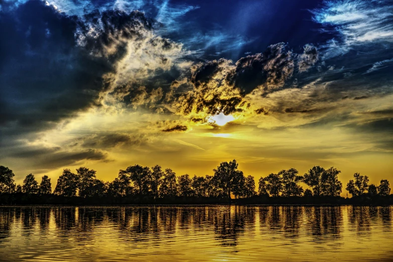 a large body of water under a cloudy sky, a picture, by Robert Storm Petersen, pexels contest winner, romanticism, dappled golden sunset, trees reflecting on the lake, yellow and blue, stunning screensaver