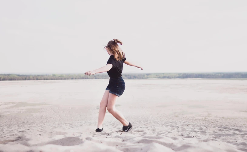 a woman standing on top of a sandy beach, pexels contest winner, happening, dancing a jig, wearing black shorts, maisie williams, an aesthetic!