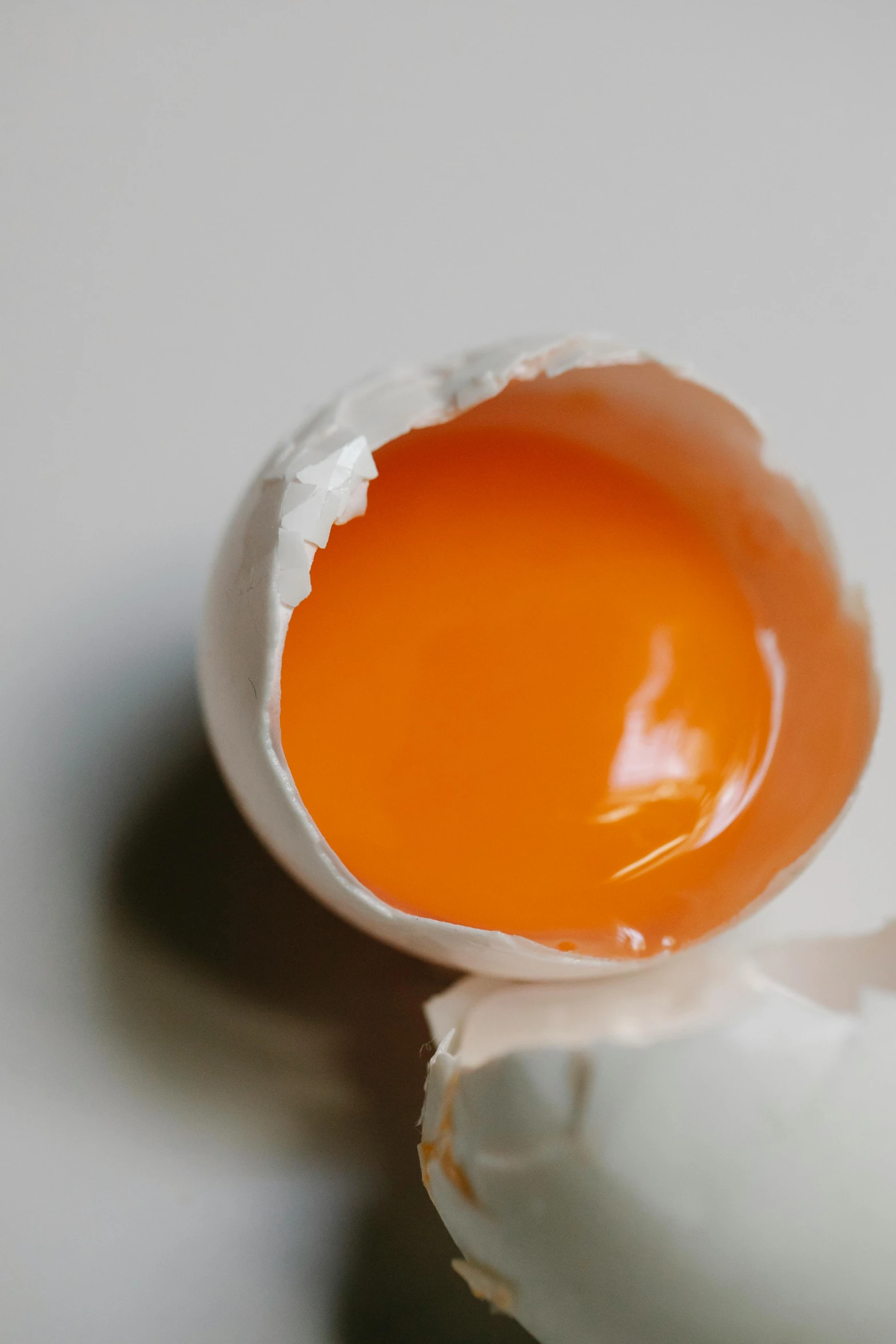 a broken egg sitting on top of a table, light orange values, oily sheen, zoomed in, opening shot