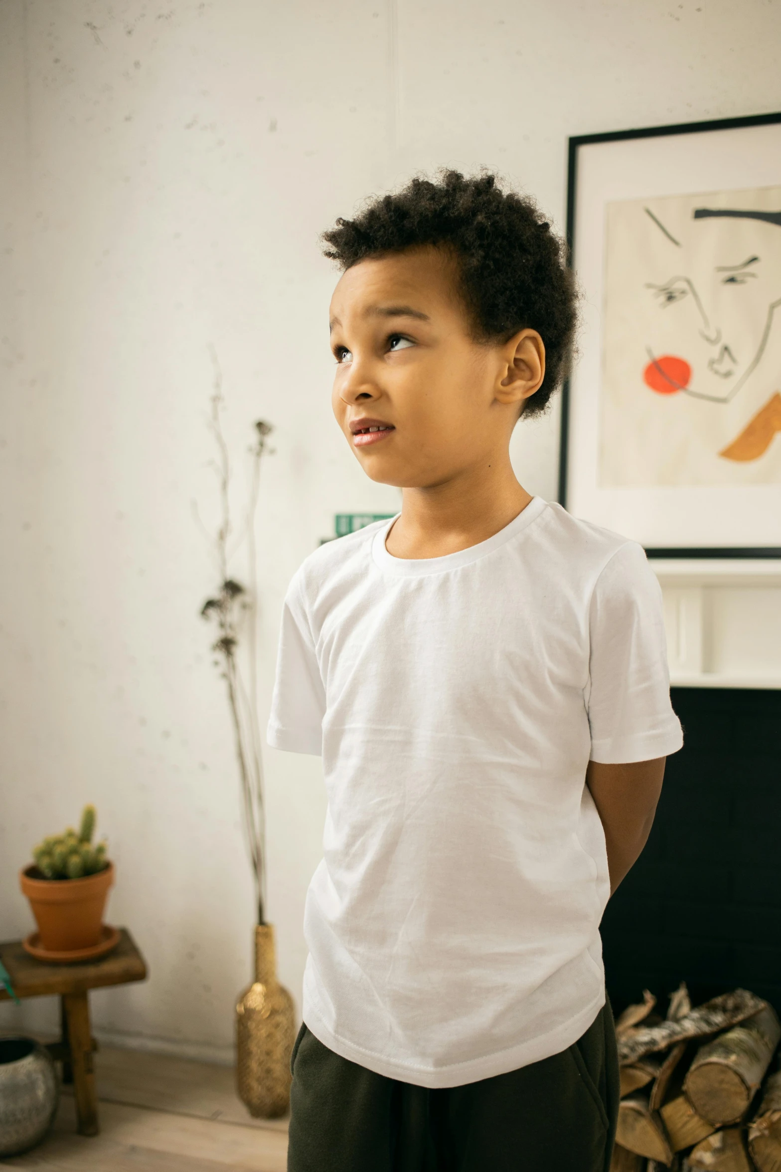 a young boy standing in front of a fire place, dressed in a white t shirt, looking off to the side, wide neck, no - text no - logo