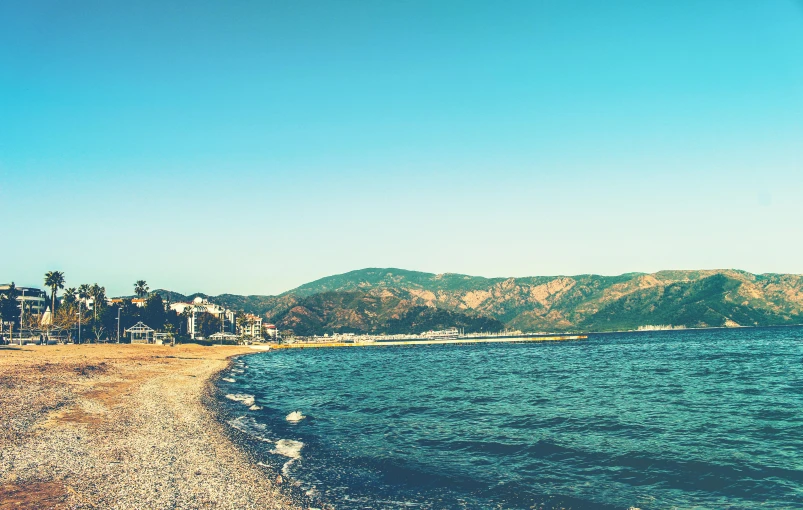 a view of a beach with mountains in the background, unsplash, baroque, genzoman, multiple stories, byzantine, clear blue sky vintage style