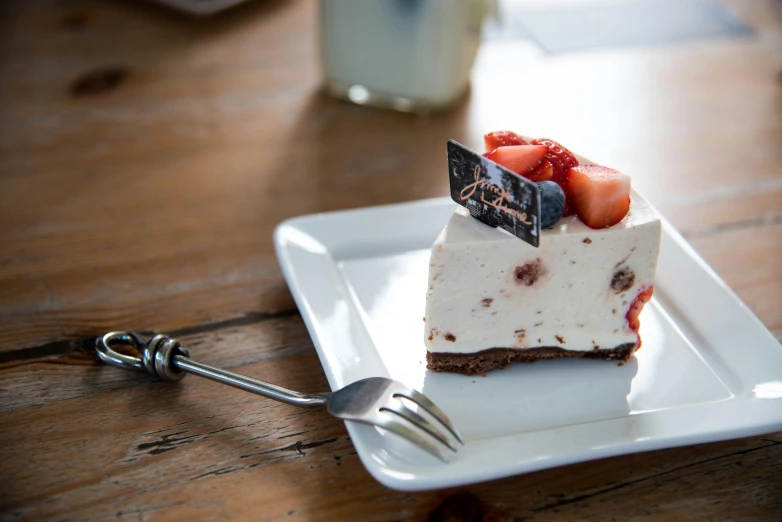 a piece of cake sitting on top of a white plate, unsplash, straya, on wooden table, background image, daily specials
