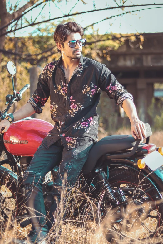 a man sitting on a motorcycle in a field, a portrait, trending on pexels, floral clothes, with kerala motifs, with sunglass, shirt