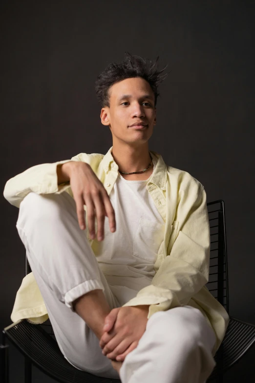 a man sitting on a chair in a yellow shirt, inspired by Barthélemy Menn, unsplash, visual art, androgynous face, wearing white cloths, mixed race, posed