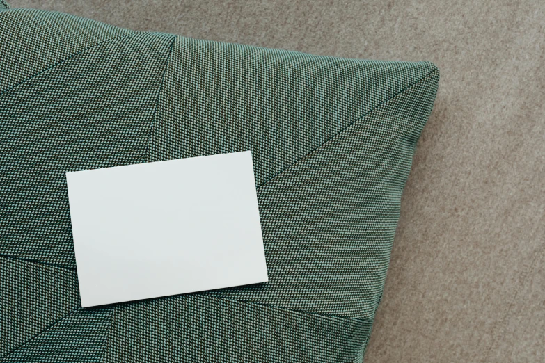 a piece of paper sitting on top of a pillow, inspired by Frederick Hammersley, unsplash contest winner, private press, white and teal metallic accents, detail shot, business card, high - angle view