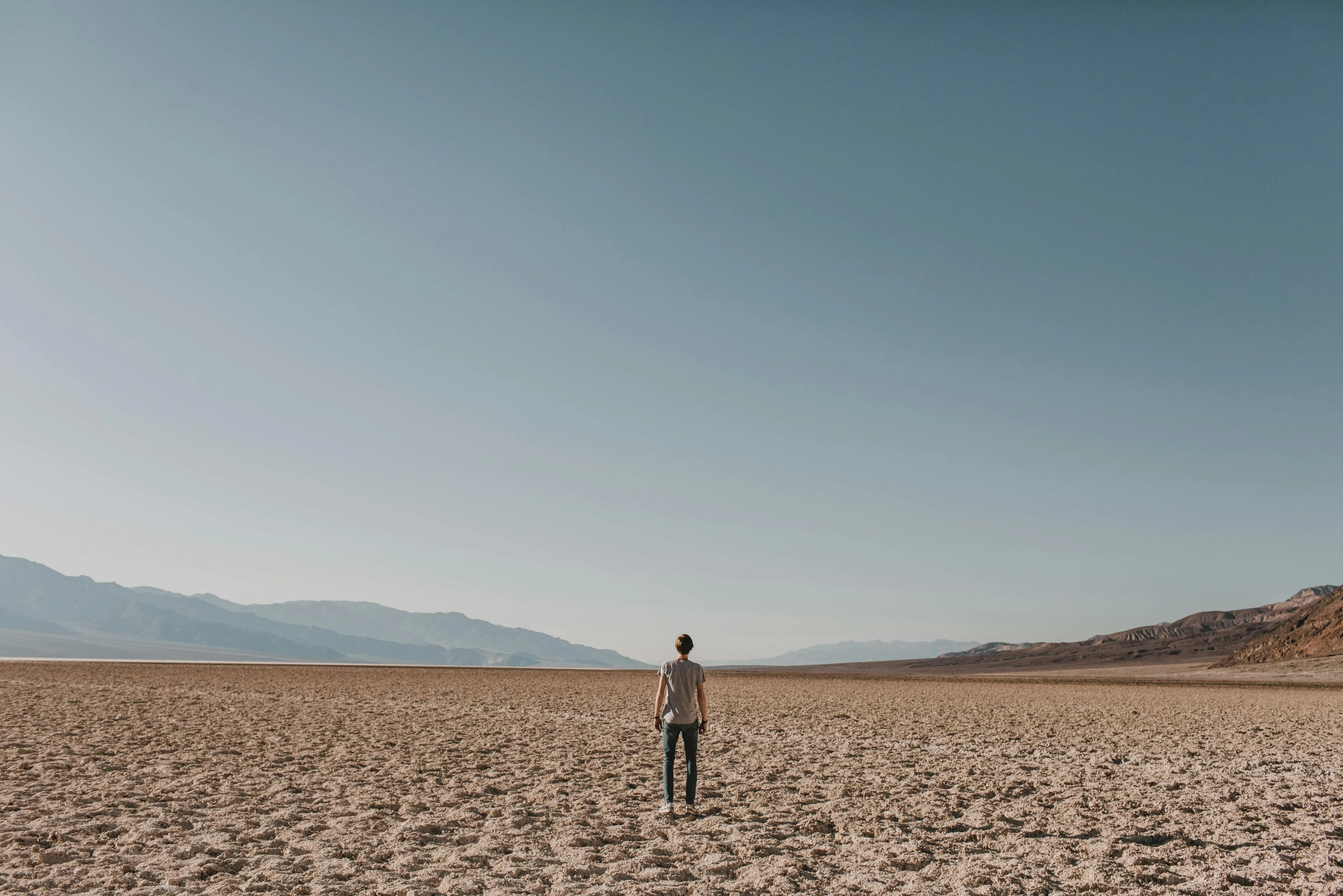 a man standing in the middle of a desert, completely empty, carson ellis, cloudless sky, from the distance