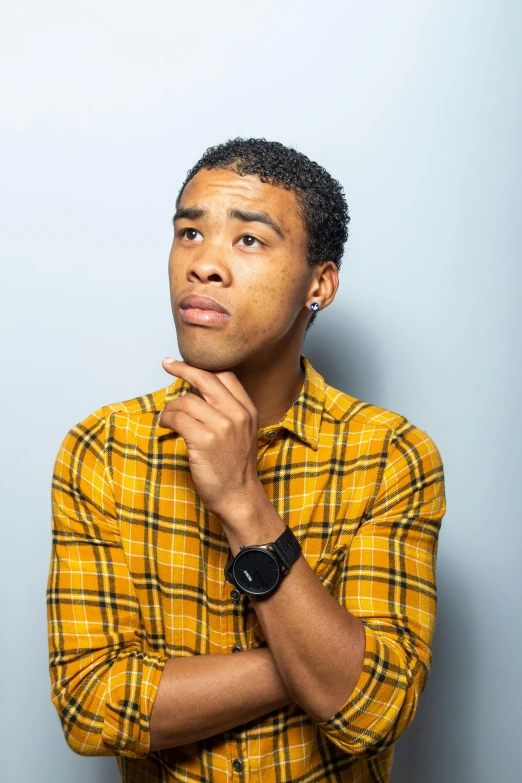 a man standing in front of a wall with his hand on his chin, by Washington Allston, pexels, non binary model, childish gambino, confused facial expression, yellow hue