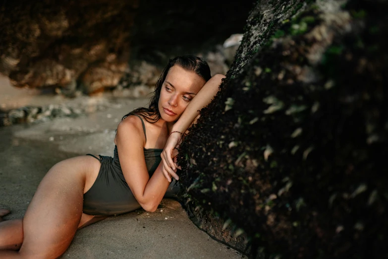 a woman laying on a beach next to a rock, a portrait, by Emma Andijewska, pexels contest winner, cute girl wearing tank suit, weathered olive skin, profile image, bali