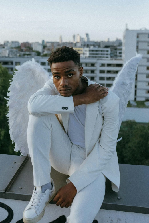 a man in a white suit sitting on top of a building, by Cosmo Alexander, pexels contest winner, renaissance, angel wings, playboi carti portrait, cupid, mkbhd