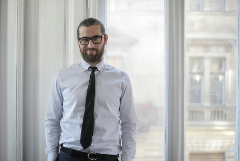 a man in a dress shirt and tie standing in front of a window, pexels contest winner, figuration libre, sebastien chabal, wearing black rimmed glasses, ceo, demna gvasalia