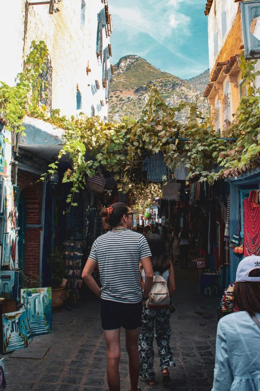 a group of people walking down a narrow street, by Julia Pishtar, trending on unsplash, mediterranean fisher village, amongst foliage, beautiful man, from the back