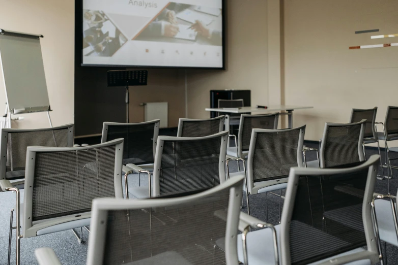 a room filled with chairs and a projector screen, by Emma Andijewska, unsplash, academic art, grey, charts, lachlan bailey, close up to the screen