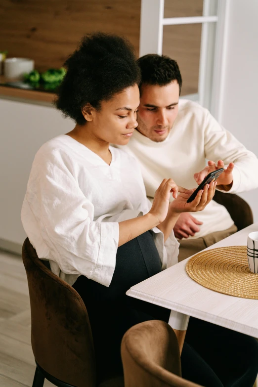 a man and woman sitting at a table looking at a cell phone