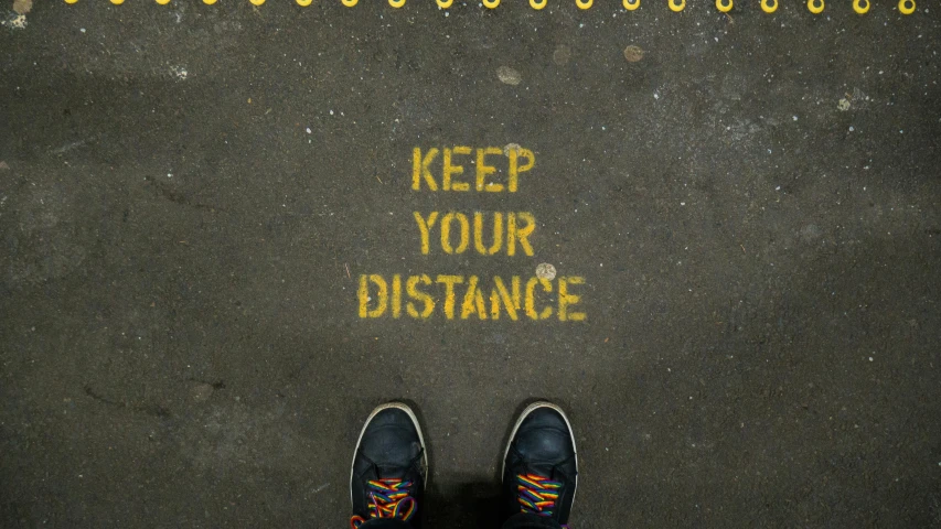 a person standing in front of a sign that says keep your distance, by Julia Pishtar, unsplash, street art, cables on floor, black and yellow, sitting on the ground, foot path