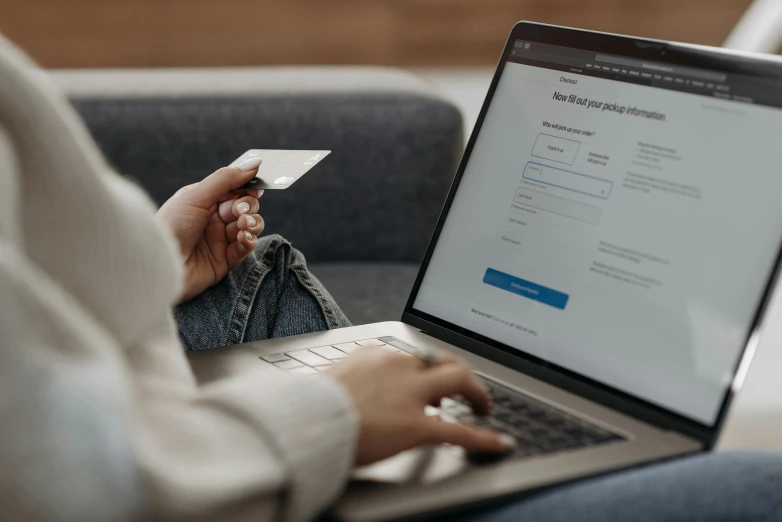 a woman sitting on a couch using a laptop with a credit card in her hand, by Carey Morris, trending on pexels, private press, worksafe. instagram photo, highly detailed rounded forms, a person standing in front of a, ux