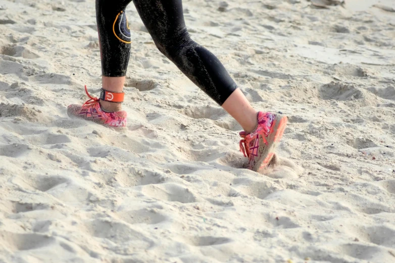 a person walking in the sand with a frisbee, running shoes, covered in coral, foot wraps, 5 k