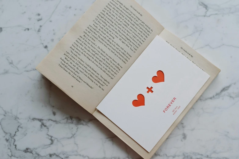 an open book with two hearts cut out of it, by Emma Andijewska, private press, on high-quality paper, light red and orange mood, library of forever, hidden message