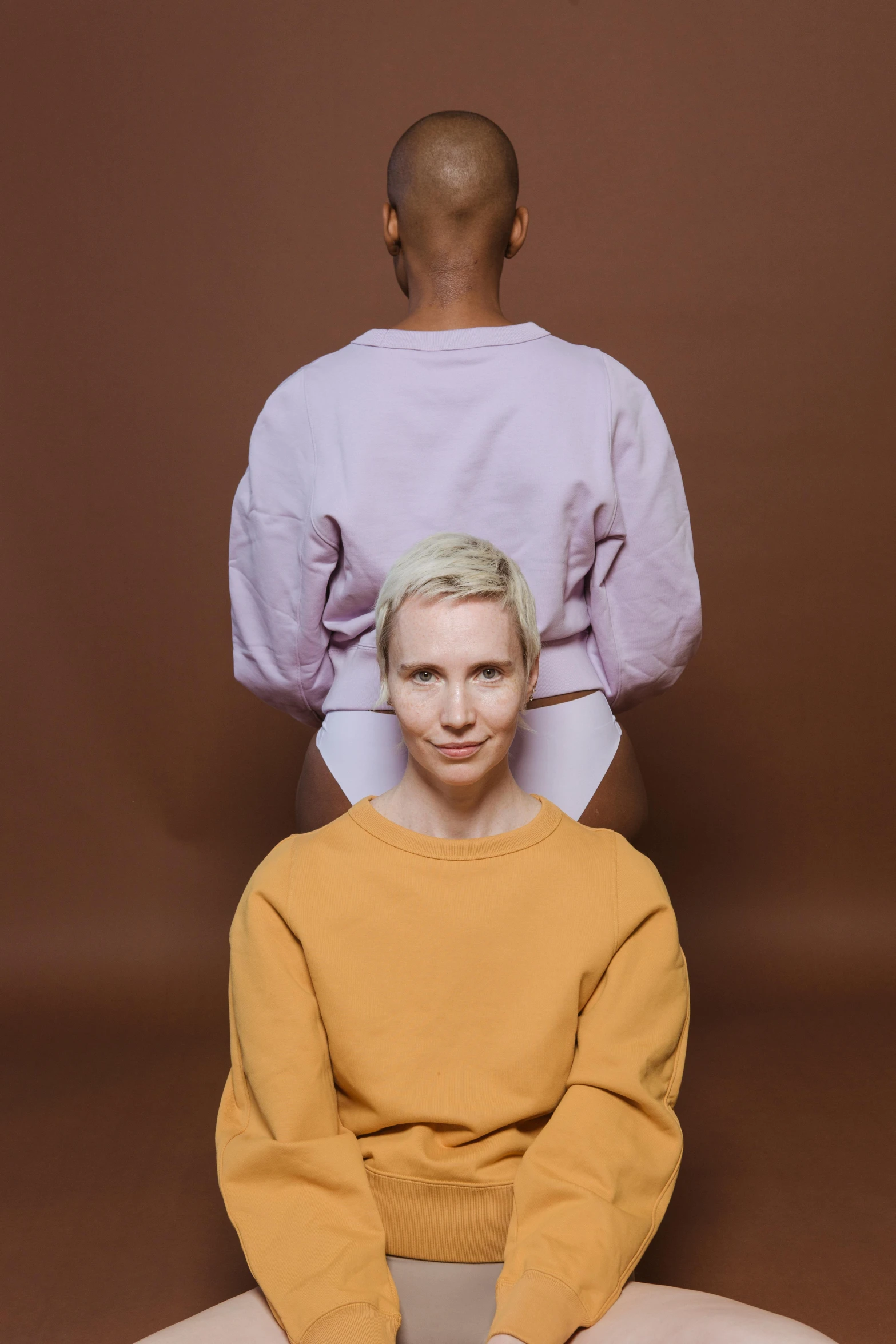 a couple of men sitting on top of each other, an album cover, by Anna Füssli, trending on pexels, portrait tilda swinton, symmetrical pose, wearing a sweater, yellow and purple tones