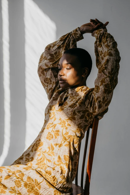 a woman sitting on top of a wooden chair, by Winona Nelson, trending on unsplash, baroque, wearing yellow floral blouse, brown skinned, wearing a dress of gossamer gold, soft shadow