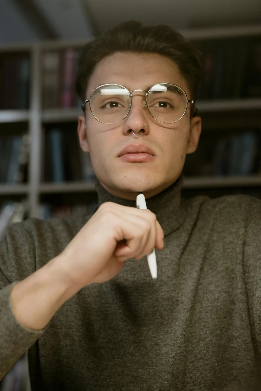 a man sitting at a table with a knife in his hand, an album cover, inspired by Oskar Lüthy, trending on tumblr, library nerd glasses, holding a syringe!!, andrea savchenko, college