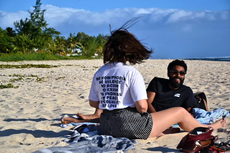 a couple of people sitting on top of a sandy beach, donald glover, printed on a cream linen t-shirt, reunion island, imaan hammam