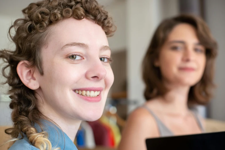 a woman sitting in front of a laptop computer, trending on reddit, pale skin curly blond hair, two women, close - up photo, subject is smiling