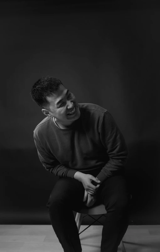 a black and white photo of a man sitting on a stool, inspired by Ding Yunpeng, mutahar laughing, portrait soft low light, 15081959 21121991 01012000 4k, like andy lau