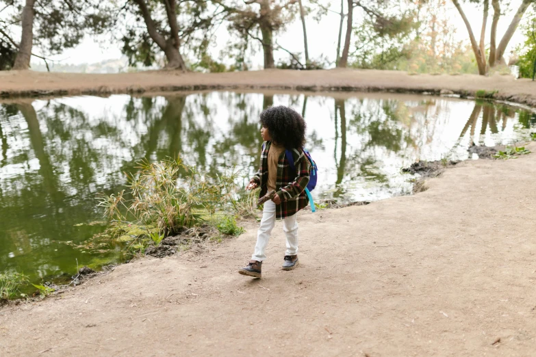 a little girl standing next to a body of water, trecking, ashteroth, at a park, wearing adventuring gear
