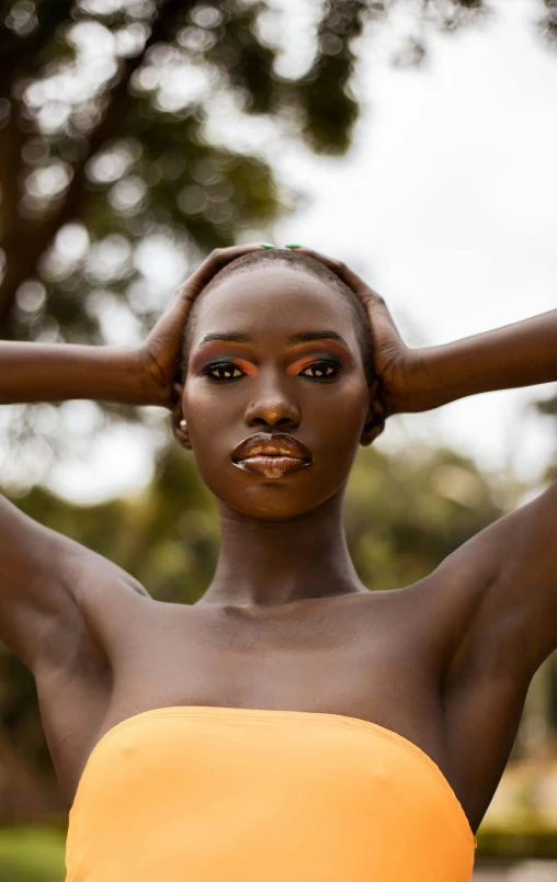 a woman in an orange dress poses for a picture, by Lily Delissa Joseph, trending on pexels, afrofuturism, brown skin. light makeup, brown:-2, adut akech, photo of a woman