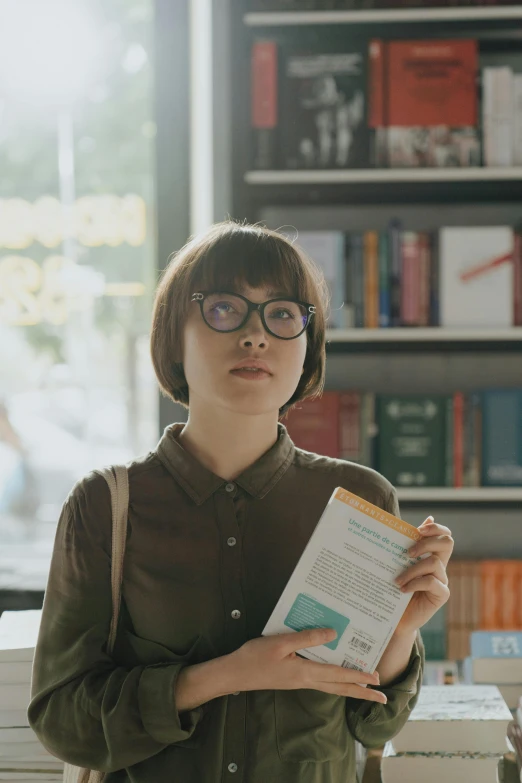 a woman standing in front of a bookshelf holding a book, by Jang Seung-eop, pexels contest winner, square rimmed glasses, kiko mizuhara, sophia lillis, commercial