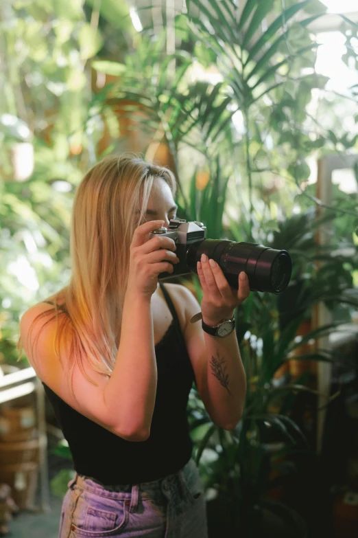 a woman taking a picture with a camera, inspired by Elsa Bleda, lush surroundings, profile image, indoor picture, plants