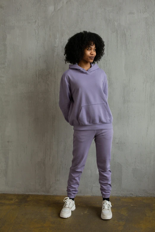 a woman standing in front of a concrete wall, inspired by Itō Seiu, unsplash, renaissance, wearing a purple sweatsuit, wearing a hoodie and sweatpants, pastel clothing, thumbnail