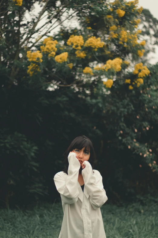 a woman standing on top of a lush green field, an album cover, unsplash, romanticism, white and yellow scheme, flowers in her dark hair, white sleeves, at a park