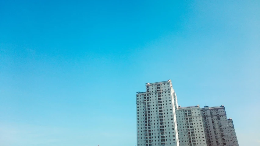 a man flying a kite on top of a sandy beach, pexels contest winner, minimalism, soviet apartment buildings, clear blue sky, three towers, south jakarta