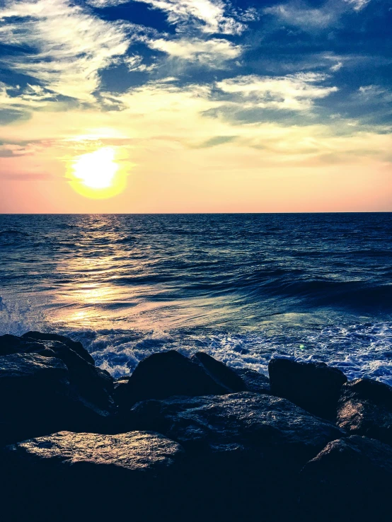 a sunset over the ocean with rocks in the foreground, looking sad, on a sunny day, stunning screensaver, multiple stories