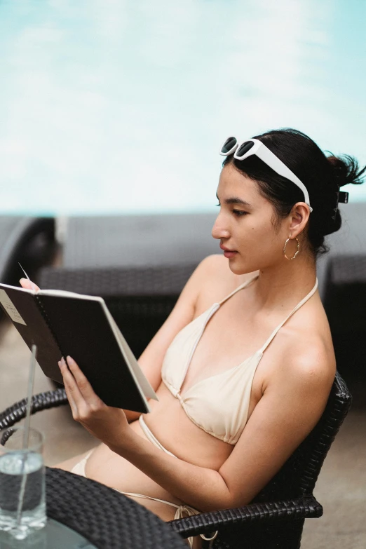 a woman sitting in a chair reading a book, pexels contest winner, wearing two - piece swimsuit, gemma chan, sketching, infp young woman