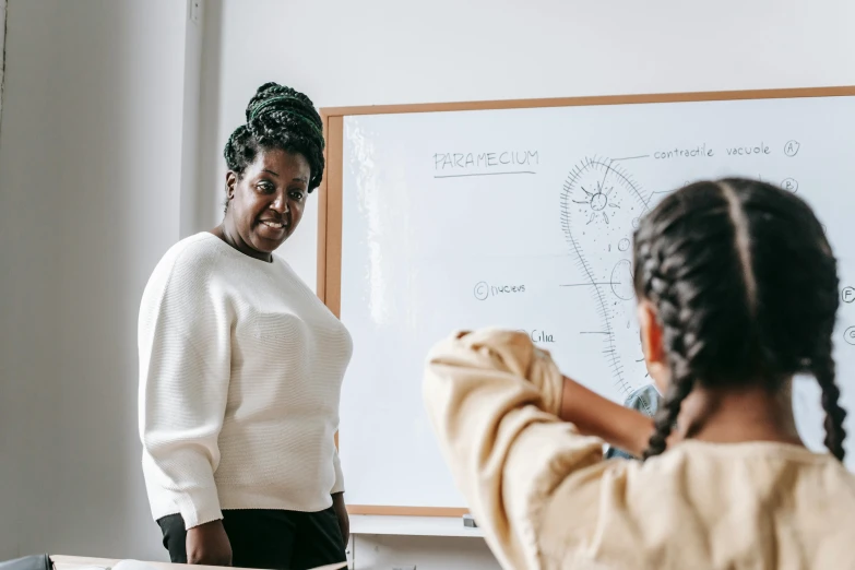 a woman standing in front of a whiteboard in a classroom, by Arabella Rankin, pexels contest winner, brown skinned, smiling at each other, thicc, thumbnail