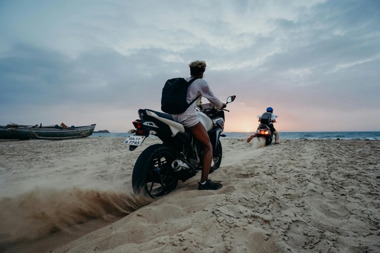 a man riding a motorcycle on top of a sandy beach, pexels contest winner, avatar image, back to back, woman, late evening