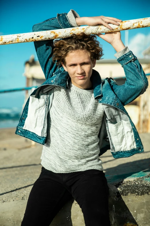 a man holding a pole over his head, an album cover, by Jacob Toorenvliet, happening, portrait of a rugged young man, standing near the beach, pale skin curly blond hair, wearing casual clothing