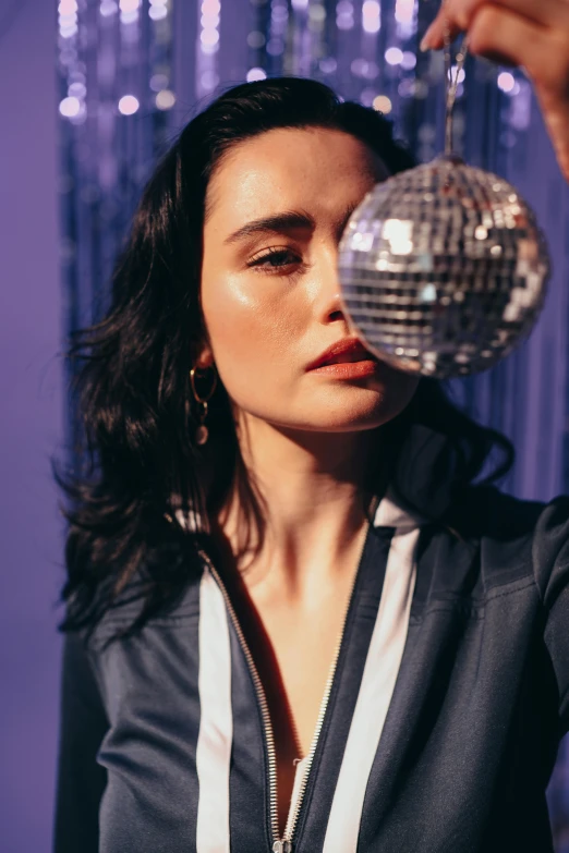 a woman holding a disco ball in front of her face, an album cover, trending on pexels, photorealism, ana de la reguera portrait, wearing a track suit, indigo, looking away