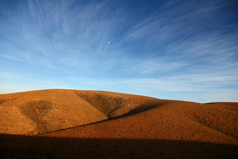 a hill in the middle of a desert under a blue sky, by Peter Churcher, unsplash contest winner, australian tonalism, crescent moon, red ocher, july 2 0 1 1, late afternoon sun