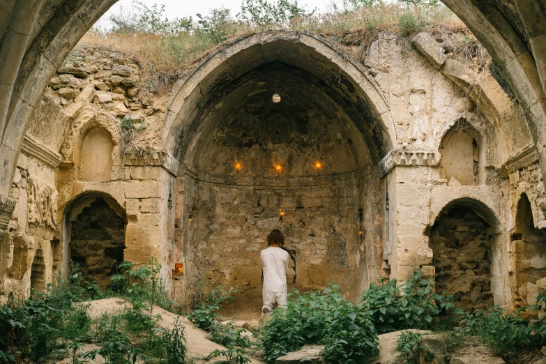 a person standing inside of a stone building, lush surroundings, orthodox, dry archways, full body image