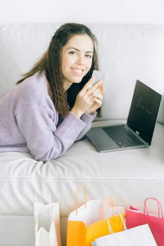 a woman laying on a couch with shopping bags and a laptop, a colorized photo, trending on pexels, pastel', lovingly looking at camera, young woman with long dark hair, programmer