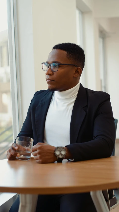 a man sitting at a table with a glass of wine, wearing black rimmed glasses, dark skinned, non-binary, profile image