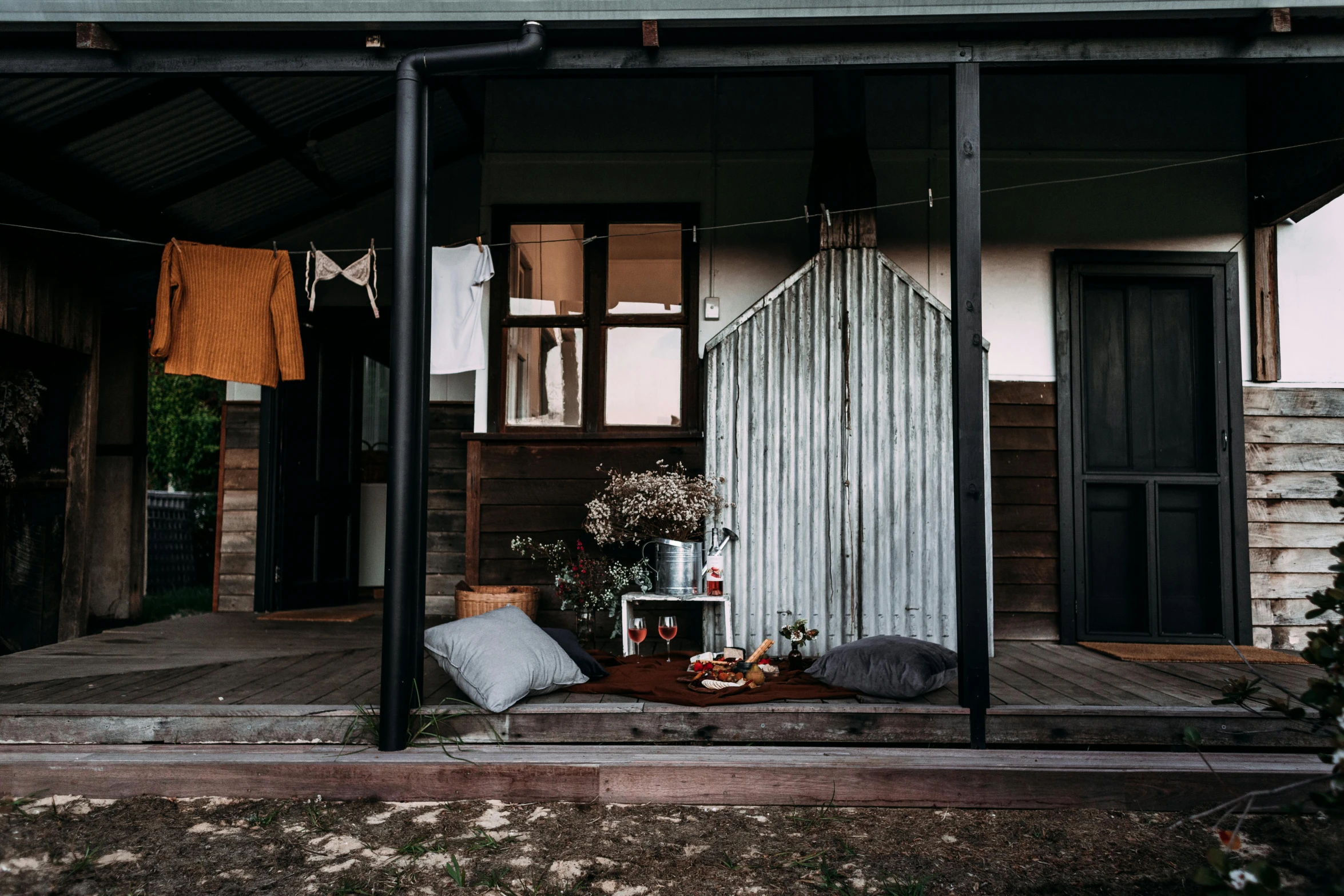 a porch with a table and pillows on it, by Lee Loughridge, unsplash, minimalism, stood outside a wooden cabin, “ iron bark, doors to various living quarters, drenched clothing