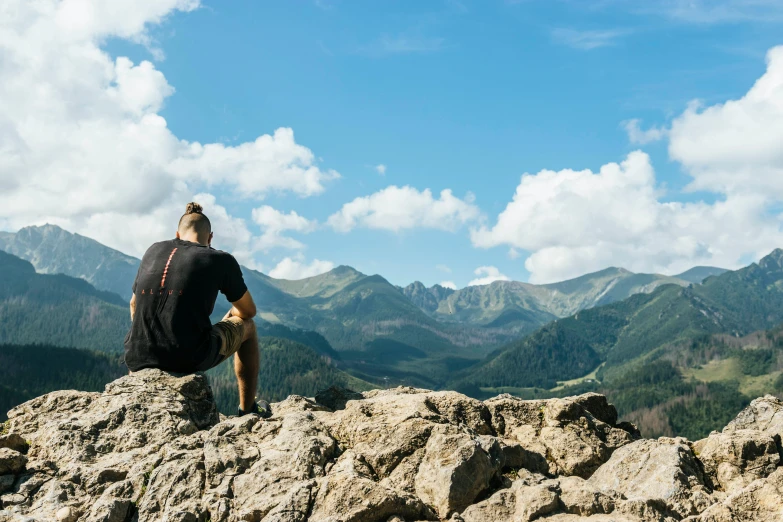 a man sitting on top of a large rock, by Adam Marczyński, pexels contest winner, looking at the mountains, profile image, thumbnail, multiple stories