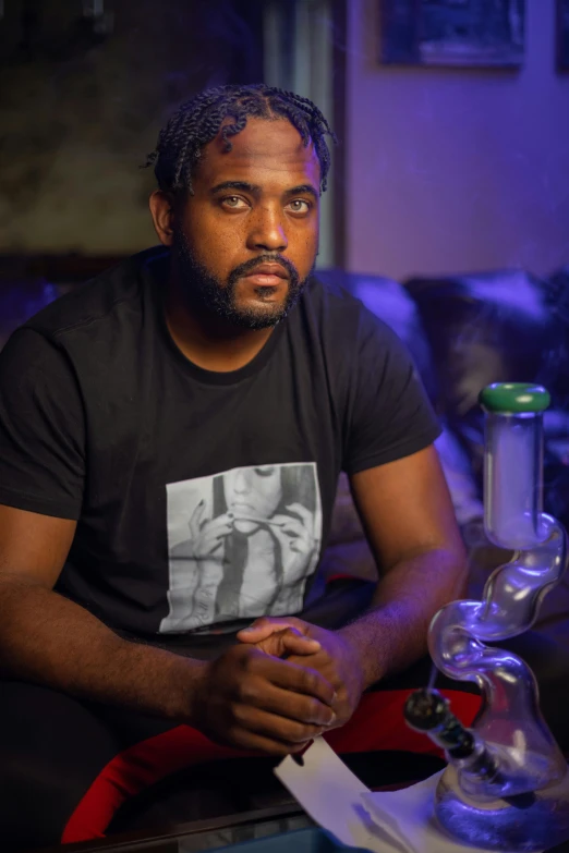 a man sitting at a table in a dark room, a portrait, featured on reddit, ganja, on a couch, riyahd cassiem, press shot