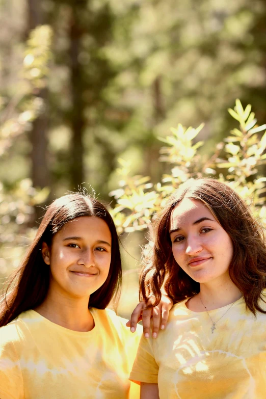 two girls standing next to each other in a forest, wearing a modern yellow tshirt, portrait image, slide show, jaime jasso